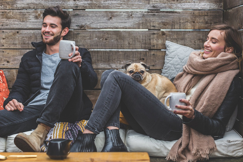 smiling couple sitting down holding mugs with bulldog