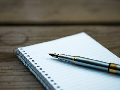 A silver fountain pen on a lined notepad.