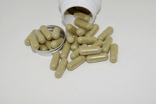 Capsules filled with green powder spilling out of a white bottle.