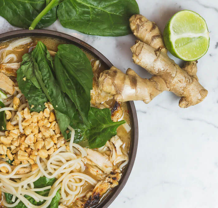 Root ginger and half a lime next to a plate of cooked noodles and spinach